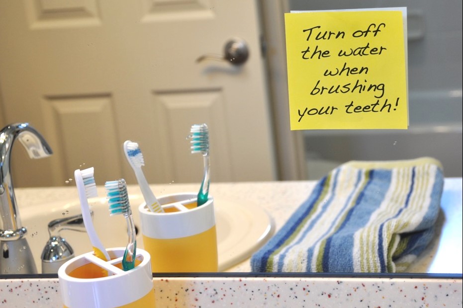 Image of toothbrush on sink with reminder note on mirror to turn off water when brushing teeth.